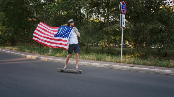 Stylish Young Male in Glasses and Hat is Holding Waving Flag of USA and Demonstrating It Riding