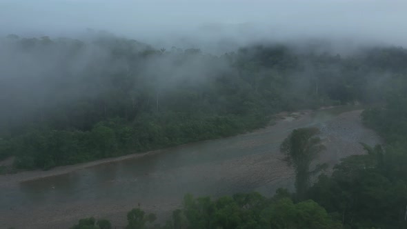 Drone shot flying through mist and revealing a large tropical river that is covered in pebbles