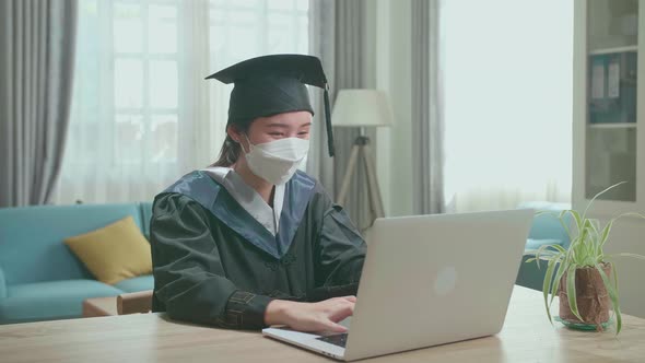 Asian Woman Wear Protection Mask And Wear A Graduation Gown And Cap Use Laptop Computer