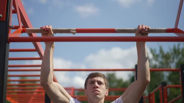 Front View Serious Sportsman Doing Pull Ups on Gymnastics Bar in Sunlight Outdoors