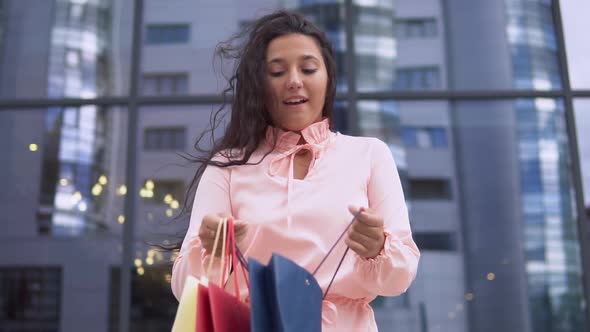 A Young Girl in a Pink Dress After Shopping with Bags in Her Hands is Happy with the Purchases