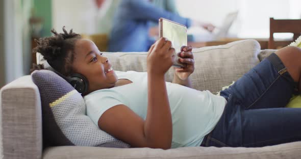 Happy african american girl lying on sofa using tablet