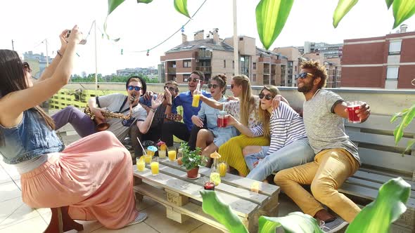 Beautiful girl taking photos of smiling friends on a rooftop terrace