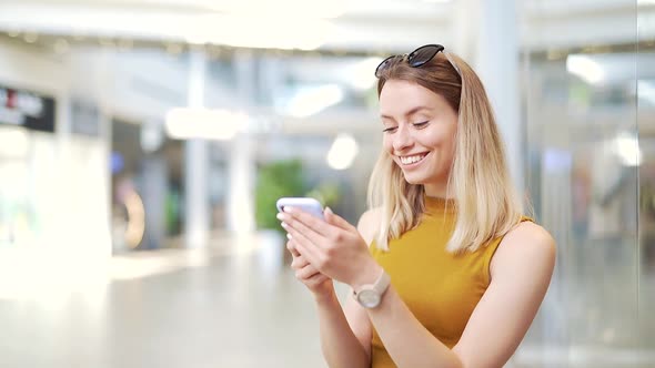 Young woman consumer in the mall browses chat and uses using a smartphone.