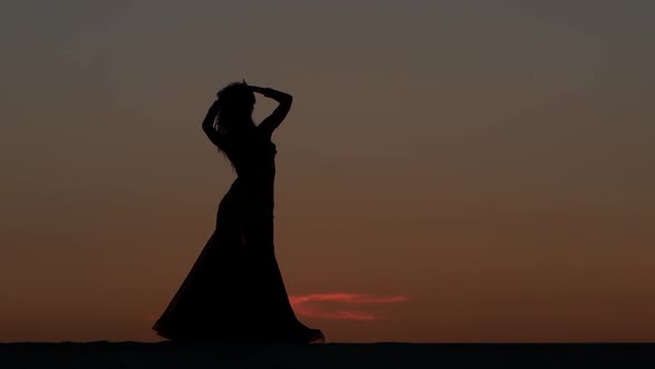 Girl Is Dancing Belly Dancing Against the Beautiful Sunset on the Beach. Silhouettes