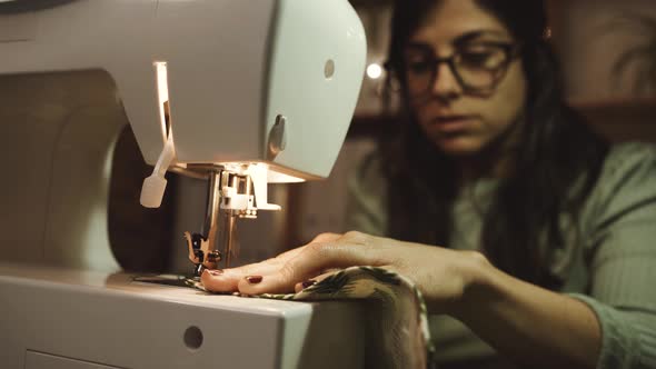 Crop seamstress pulling out thread of sewing machine in atelier