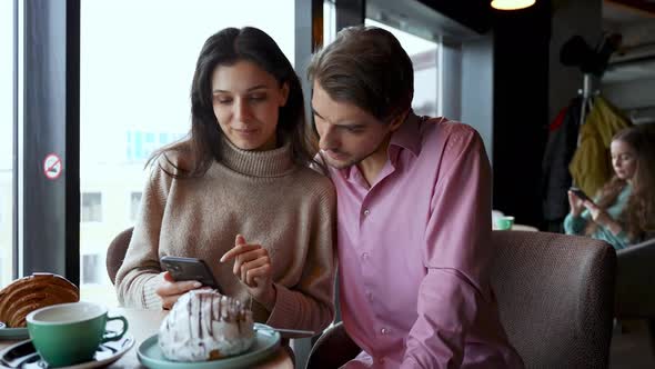 Couple in the Cafe Holding Smartphone Celebrate Online Betting Victory