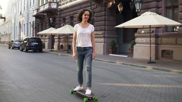 Attractive Brunette Woman in White Tshirt Blue Jeans and White Sneakers Skateboarding at Sunrise in