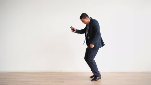 Happy Male Office Worker in Formal Clothes Uses Mobile Phone Rejoices in Victory