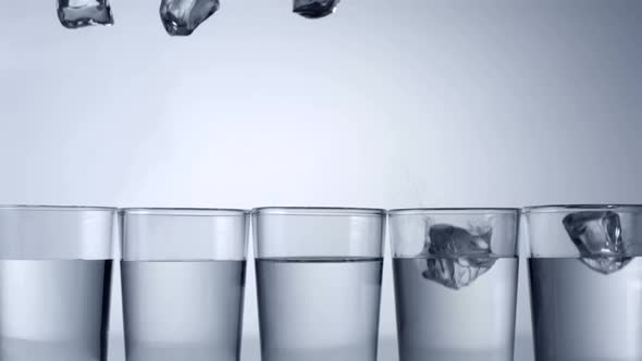 Slo-motion ice cubes falling into row of glasses, one misses