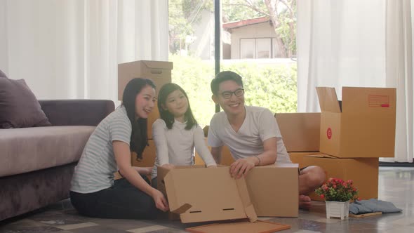 Chinese parents and kids open cardboard box or parcel unpacking in living room on moving day.