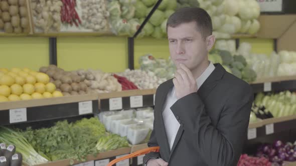 Portrait of Brunette Caucasian Man with Brown Eyes Standing in Grocery and Thinking. Serious Guy in