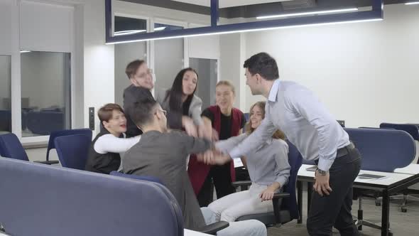 Wide Shot of Cheerful Men and Women Stacking Hands Rejoicing Business Success in Office Indoors