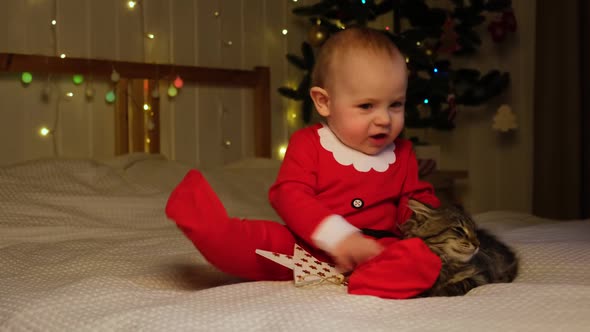 Christmas Baby in Red Santa Costume Sitting on White Soft Bed