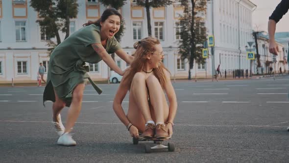 Teenage Friends Having Fun Together. Blonde Girl Sitting on Longboard and Another Asian Woman