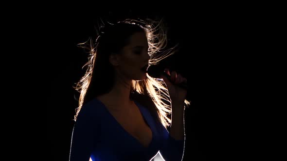 Girl in the Blue Frank Top Sings Into the Microphone. Black Background. Silhouette