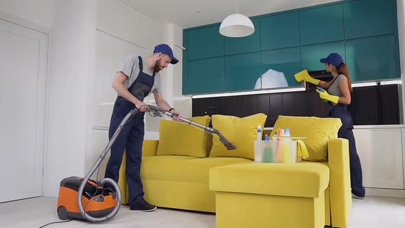 Workers from Cleaning Service Where Man Vacuuming the Sofa and Woman Wiping a Furniture