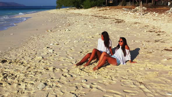 Pretty smiling ladies relaxing in the sun on the beach on summer white sandy and blue 4K background