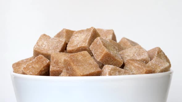 Unrefined Sugar Pieces in Bowl Rotating Close-Up on White Background