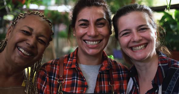 Multiracial women working together inside nursery greenhouse while smiling on camera