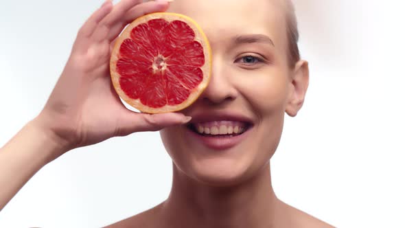 Woman Smiles Closing Eye with Round Slice of Citrus Fruits Containing Vitamins Useful for Skin