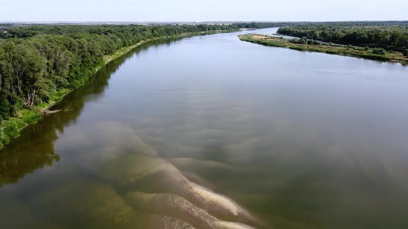 Beautiful river with green trees on the shore. Big sand dunes under transparent water