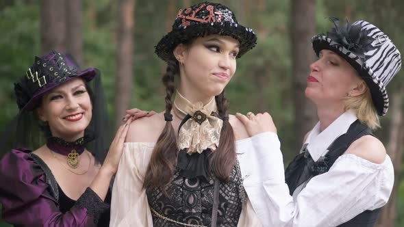 Adult Women Admiring Young Slim Gorgeous Lady with Steampunk Makeup Standing in Forest