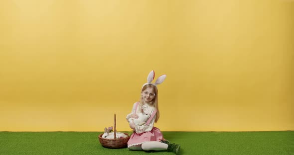 Little Girl in a Pink Dress Holds a Basket with a Rabbit in Hand  Posing Smile