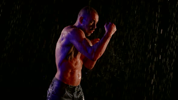 a Muscular Man with a Bare Torso Stands in the Streams of Water on a Dark Background Then Begins to