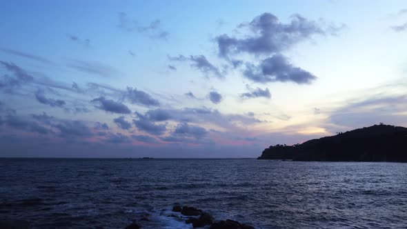 Dark island surrounded foamy waves under cloudy sky