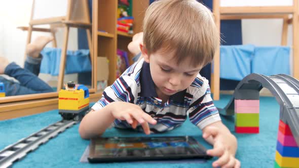 Closeup Video of Little Toddler Boy Lying on Carpet Next To Colorful Toys and Playing on Digital