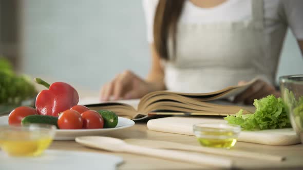 Close-Up of Girl Flipping Through Cooking Book Pages, Choosing Salad Recipe