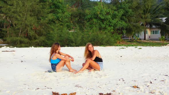Beautiful women tanning on exotic coastline beach break by blue green lagoon with bright sandy backg