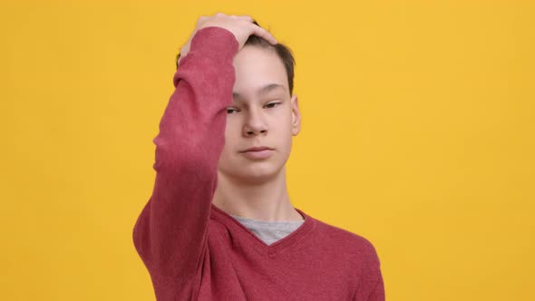 Confident Teen Boy Touching Hair Posing Over Yellow Studio Background