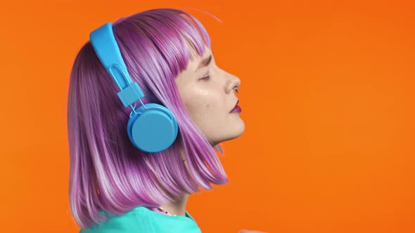 Attractive Modern Woman Dancing with Headphones on Orange Studio Background