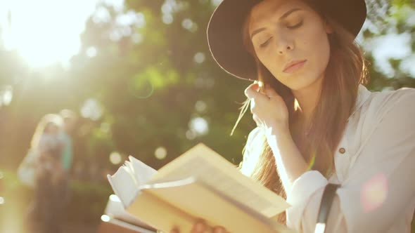 Young Beautiful Girl in Hat Reading Book in City Park