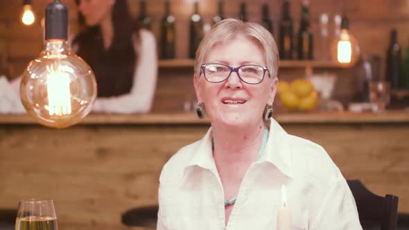 Portrait of a Beautiful Old Lady Sitting at a Table in a Bar and Talking To the Camera