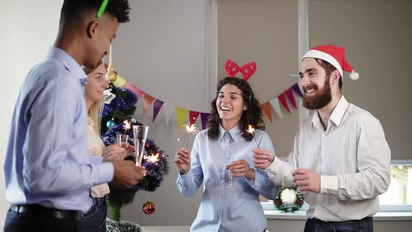 Multiethnic Group of Happy Office Workers Holding Bengal Lights and Dancing Wearing Christmas Hats