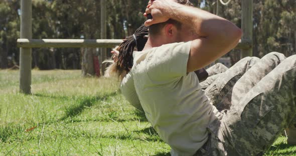 Diverse fit group of soldiers doing sit ups in field, at army obstacle course in the sun