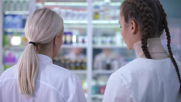 Back View Intelligent Serious Women Talking Standing in Front of Shelves in Drugstore