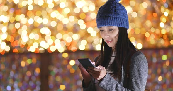 Woman look at mobile phone over christmas light decoration