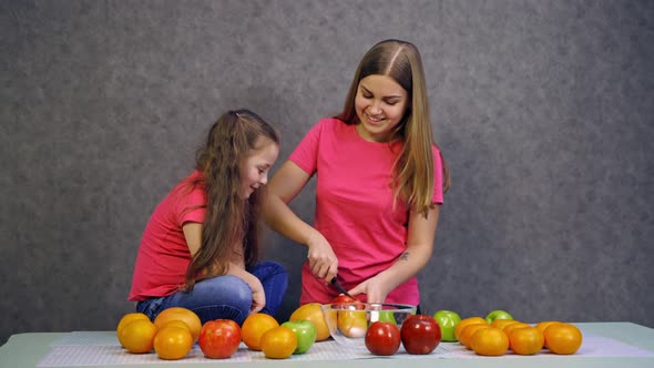 Woman cutting fruits on table. Young woman with daughter preparing healthy food