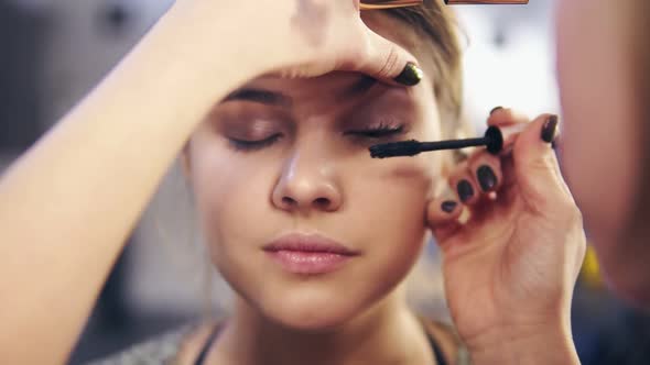 Closeup View of Professional Makeup Artist's Hands Applying Mascara on Eye Lashes of a Young