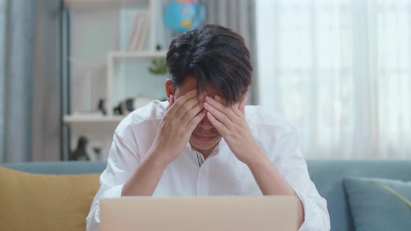 Asian Man Being Tired While Using Laptop Computer In The Living Room