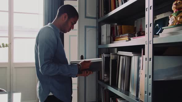 Man holding a book standing in front of a shelf in the office