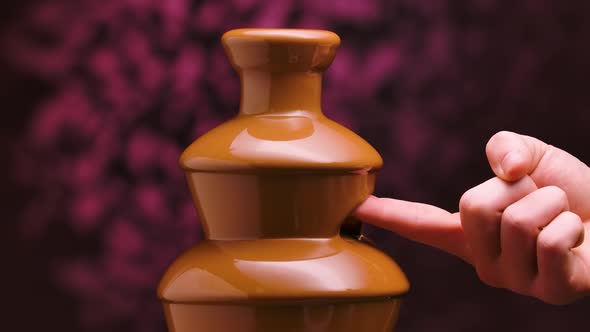 Melted Milk Chocolate Flows in a Chocolate Fountain on Blurry Purple Background