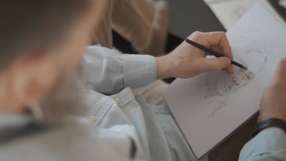 Man is sketching a face of a person on a white paper with wooden pencil.