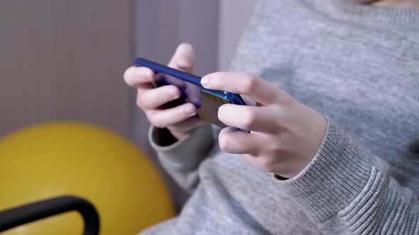 Child Sits in a Chair Holds a Smartphone in Hands Plays in Bedroom