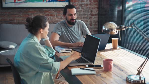 Two Coworkers are Discussing a Project While Sitting in Front of Their Laptops