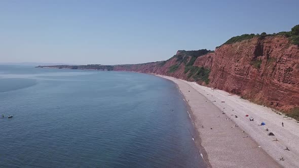 Wide shot of the red cliffs at Budleigh Salterton, Devon. Tide is in, and holiday makers are on the